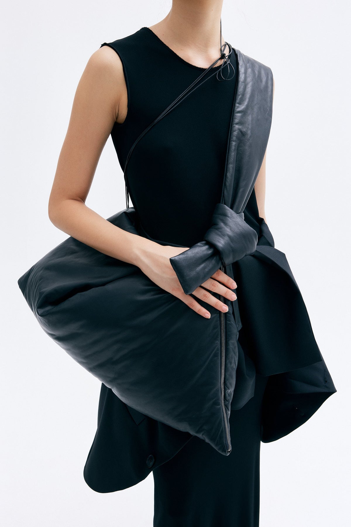 Close-up of padded black lambskin leather bag with knot handle and architectural sculptural shape.