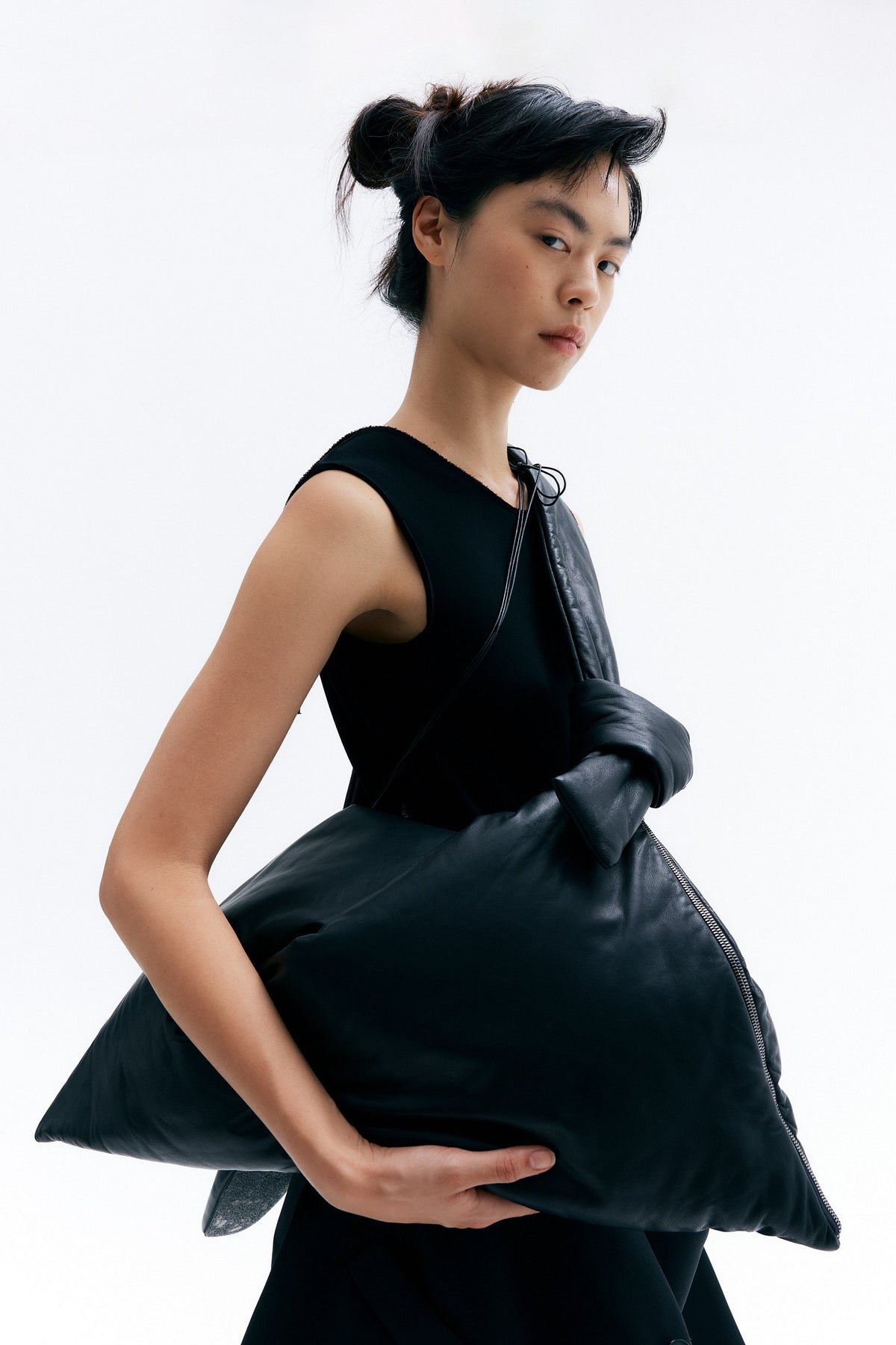 Model carrying sculptural lambskin leather bag with triangular silhouette and knot handle construction.