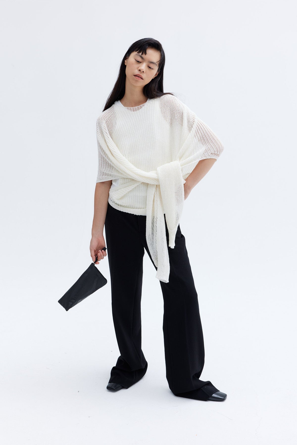 Model carrying compact padded lambskin pouch with sculptural architectural silhouette.