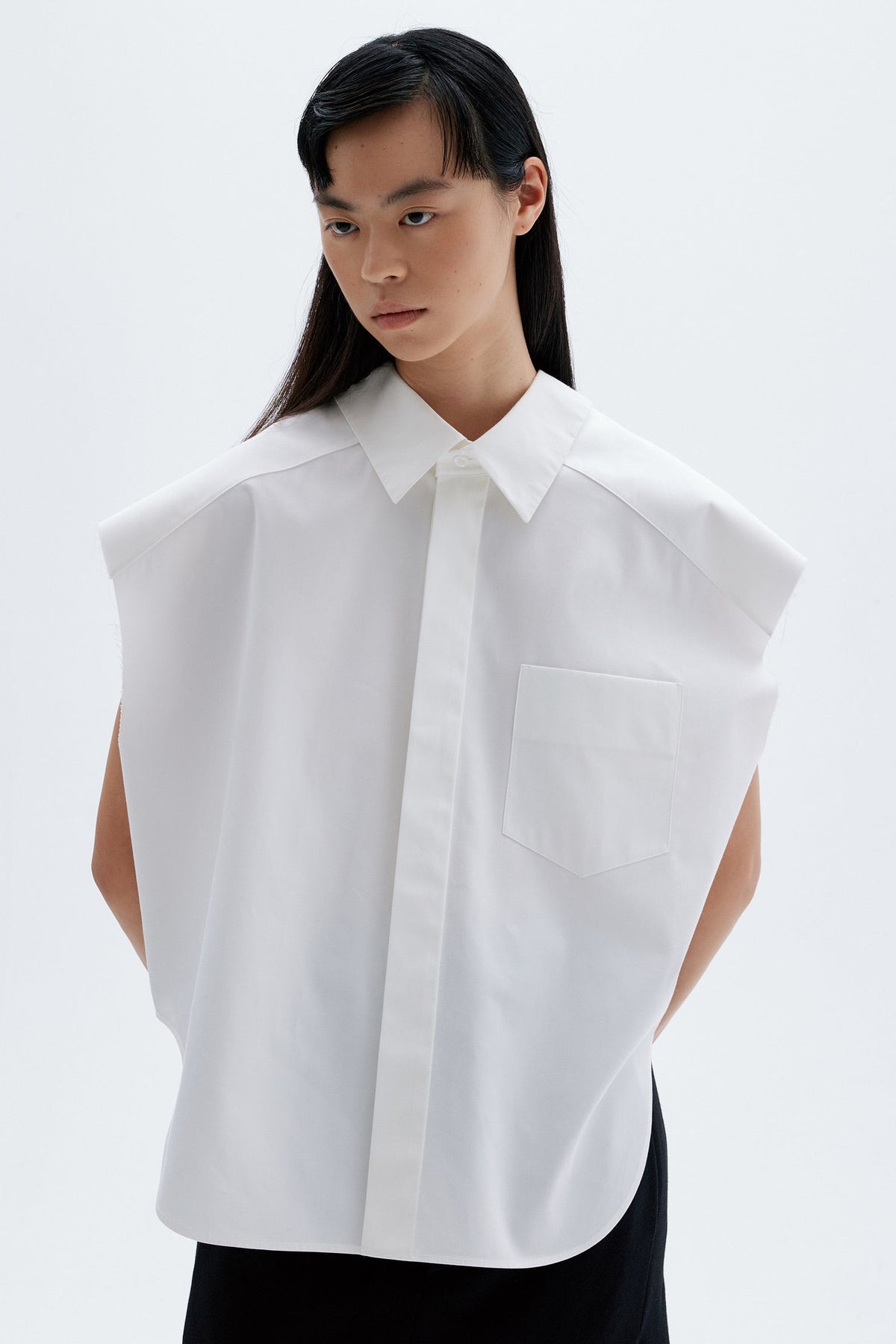 Model wearing a white sleeveless cotton shirt with a collar on a plain background