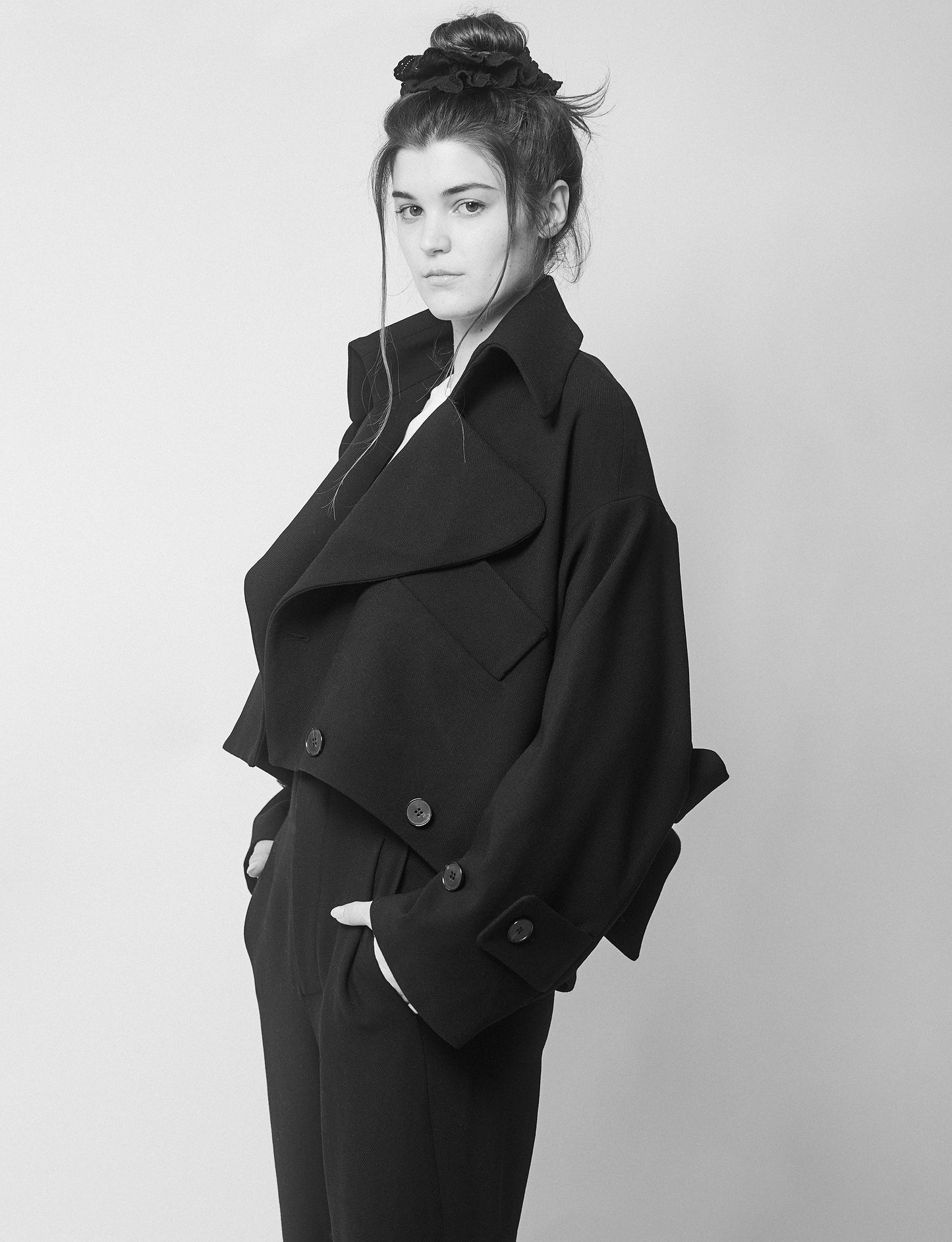 Amanda wearing a black jacket with two collars and pants on a plain background