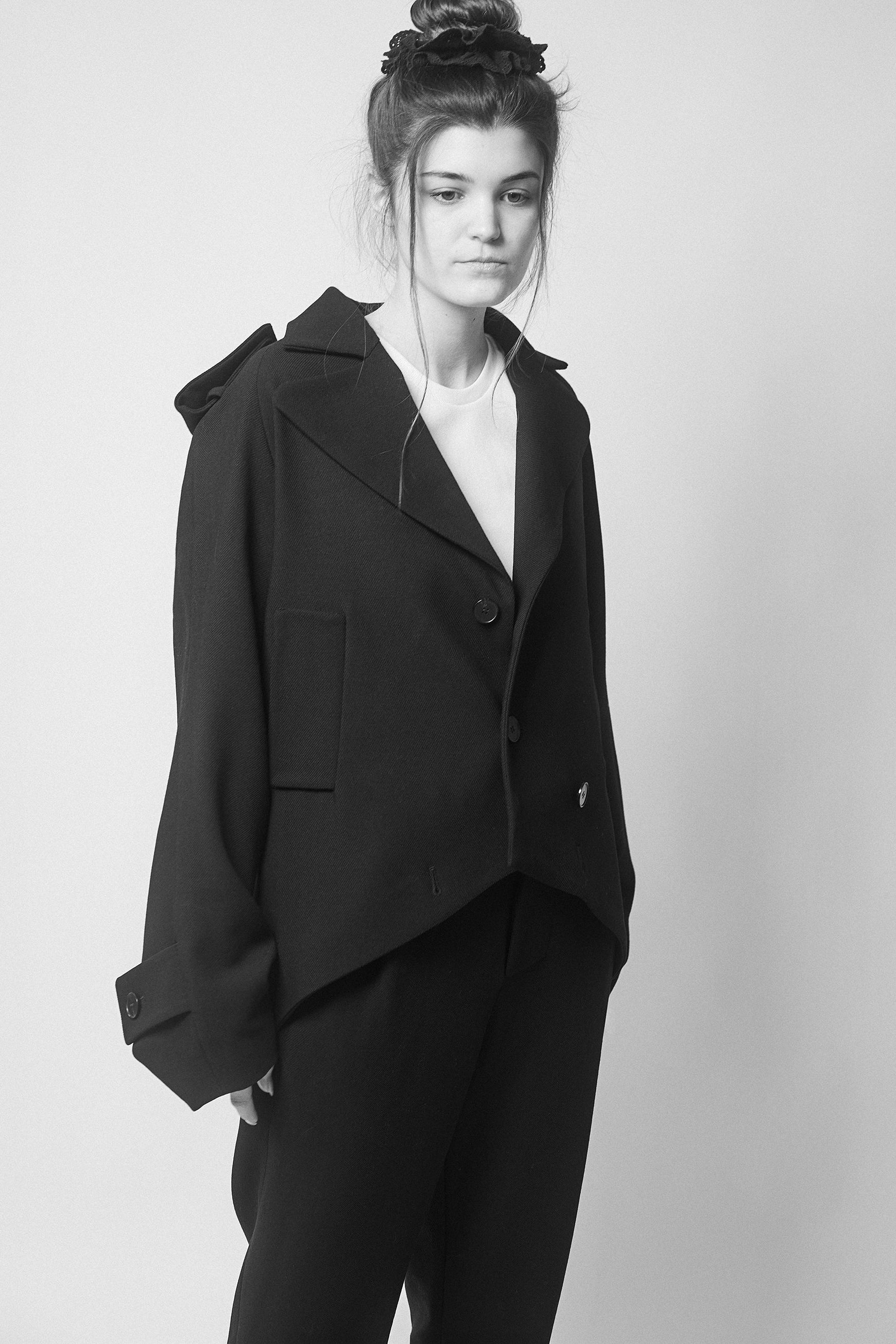 Amanda wearing a black jacket with two collars and pants against a plain background