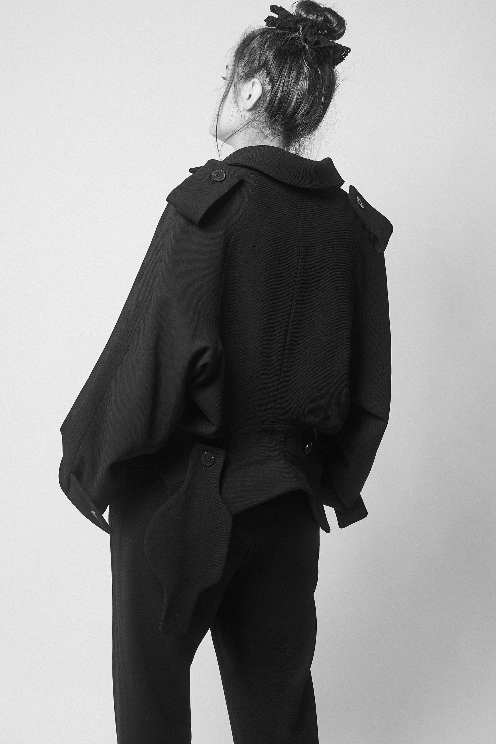 Amanda wearing a black jacket with two collars and pants against a plain background