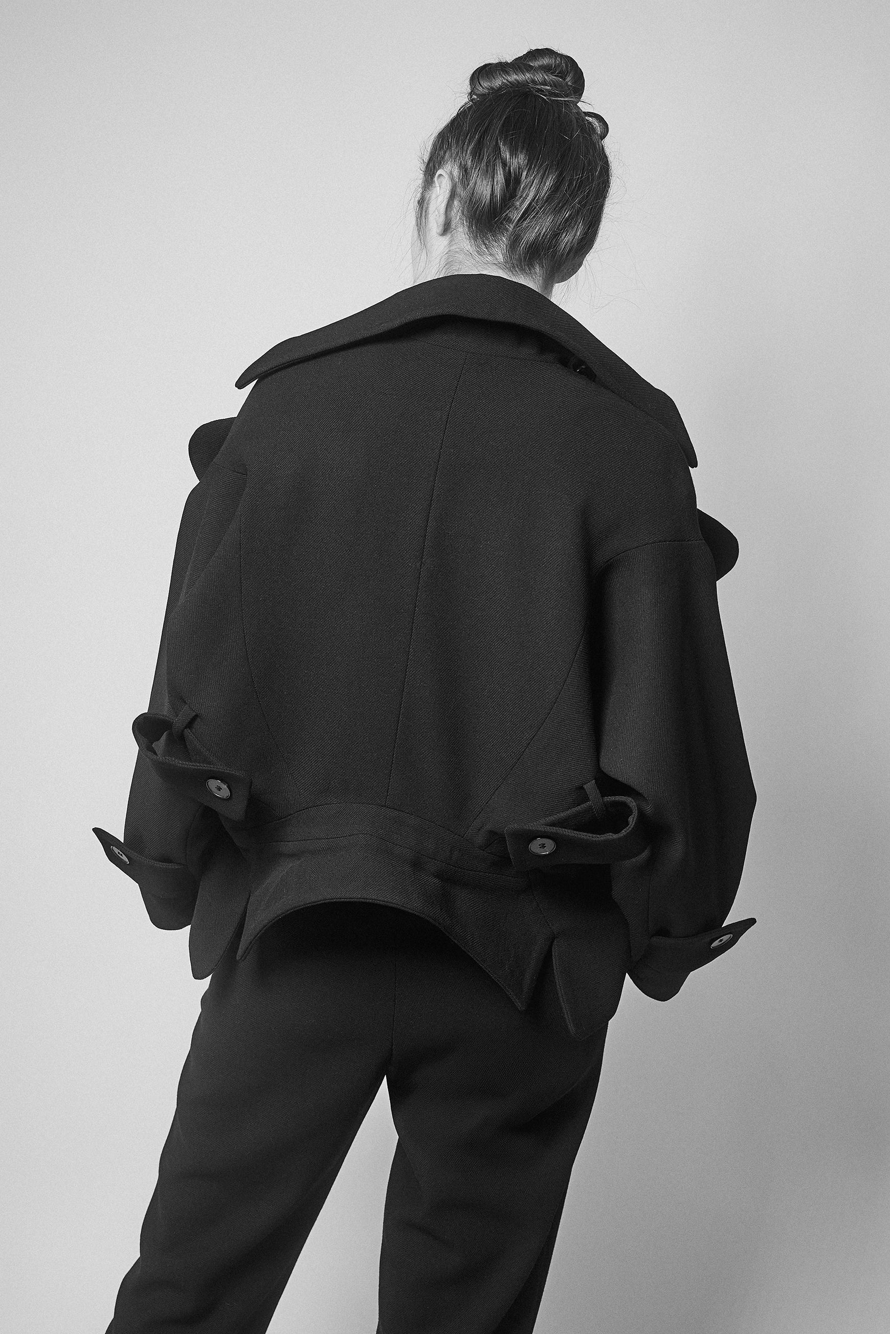 Amanda wearing a black jacket with two collars and pants against a plain background