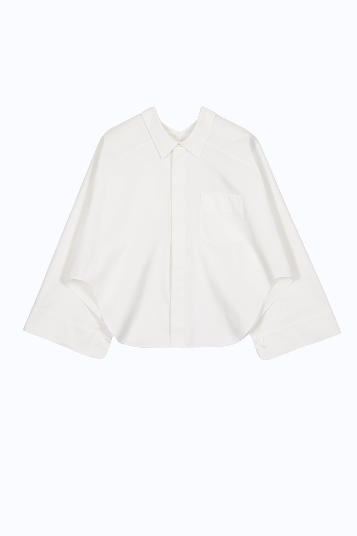 Front view of cape-inspired cotton shirt with open sleeves, patch pocket and architectural layered proportions.