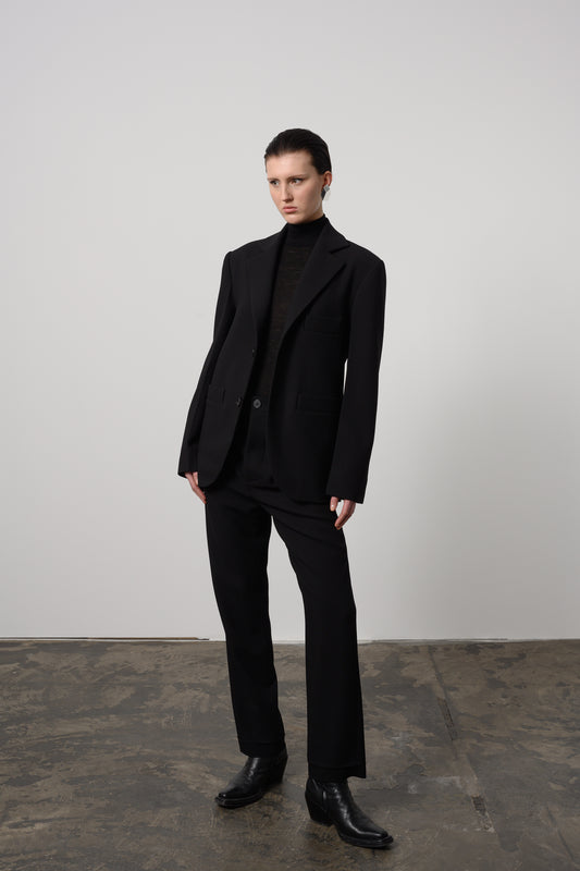 Model Zoe waers classic black oversized unisex blazer made from Italian wool, featuring notched lapels and a double-button closure for a timeless and sophisticated look.