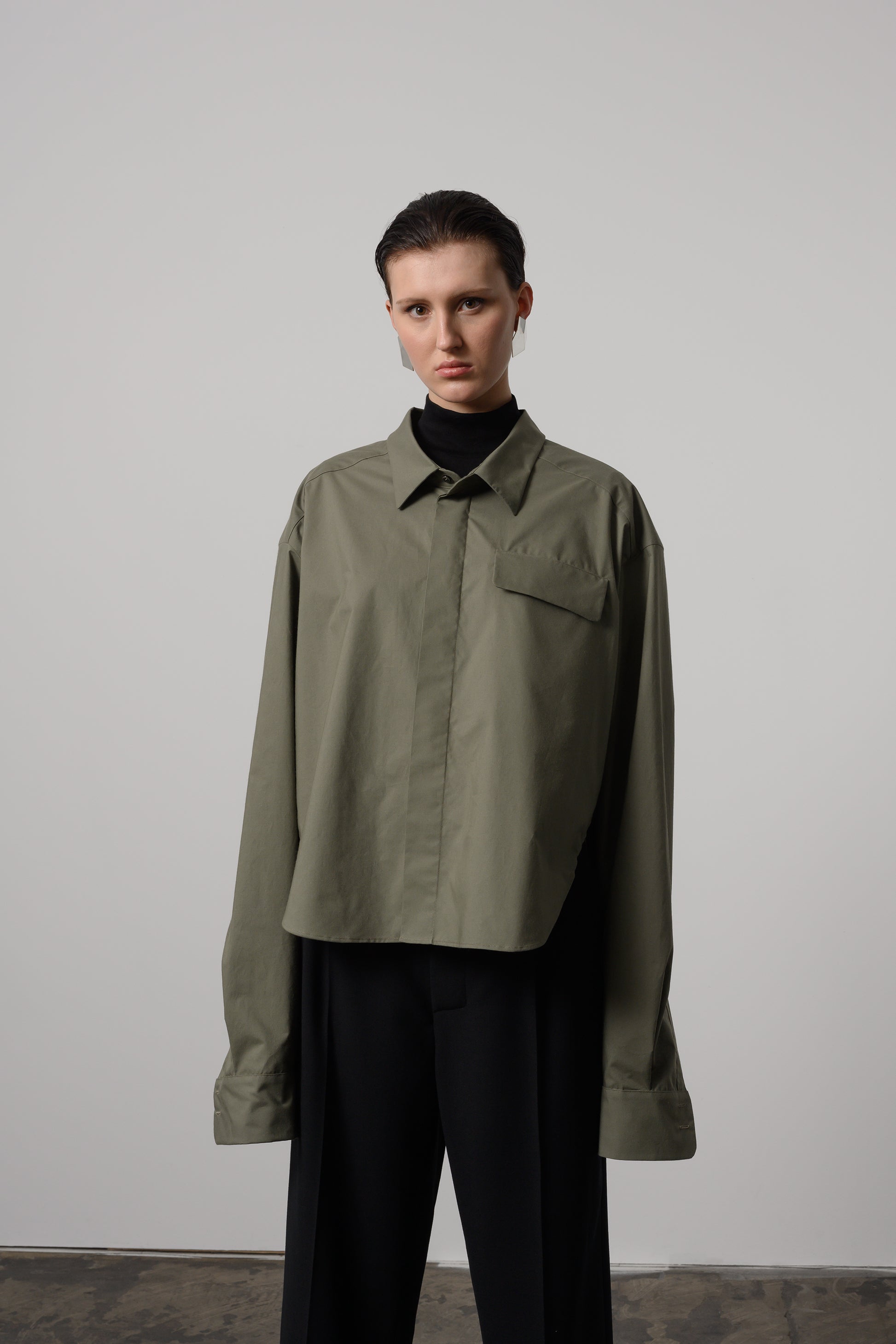 Model Zoe wearing olive green oversized shirt with classic collar and hidden button placket, made from FSC-certified cotton, styled for a casual to semi-formal look.